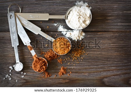 Food ingredients and kitchen utensils for cooking on a wooden board. Measuring spoons with cocoa, flour and brown sugar.