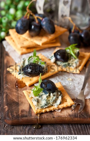 Delicious clue cheese crackers appetizer with honey and arugula on an old cooking board.