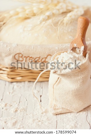 Bag of flour with wooden scoop and fresh homemade dough for bread in a basket on an old white kitchen board. Toned photo.
