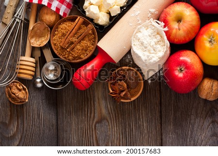 Ingredients for apple pie cooking. Fresh red apple, butter, flour, brown sugar, nuts and spices on a rustic wooden background.