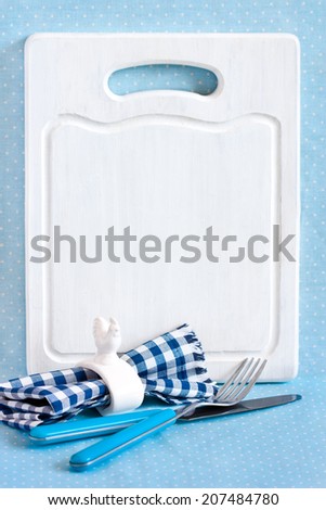 Old white kitchen cutting board with copy space for menu, cutlery set with fork and knife and napkin ring.