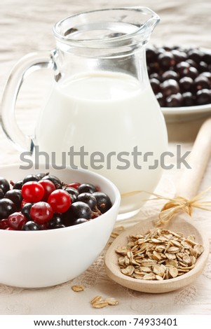 Jug of milk, berries and oat flakes on a wooden spoon.
