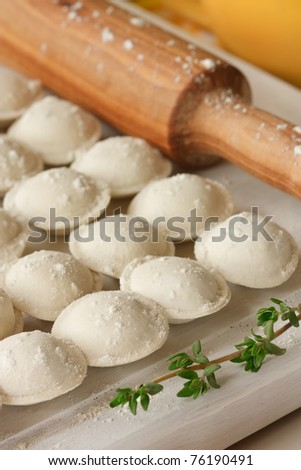 Raw pelmeni, rolling pin and thyme on a white wooden board.