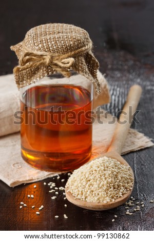 Sesame seeds on a wooden spoon and sesame oil in a glass jar.
