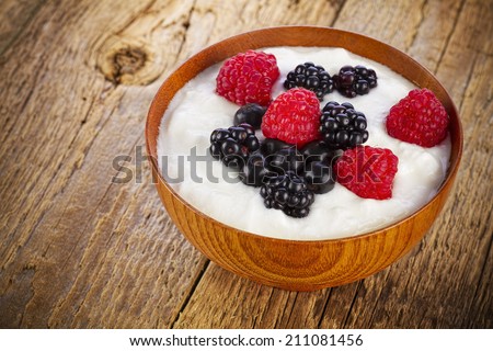 Yogurt with wild berries in wooden bowl on wooden background