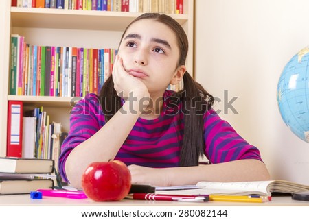Schoolgirl overwhelmed by her studies, sitting in a table full of notebooks and pencils and pens