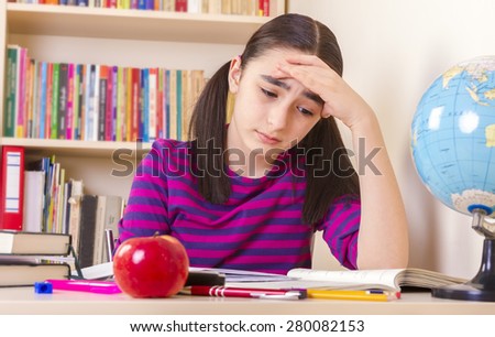 Schoolgirl overwhelmed by her studies, sitting in a table full of notebooks and pencils and pens