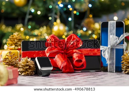 Tablet pc, smartphone and smartwatch with gifts and decorations in front of Christmas tree. Focus on smartphone.