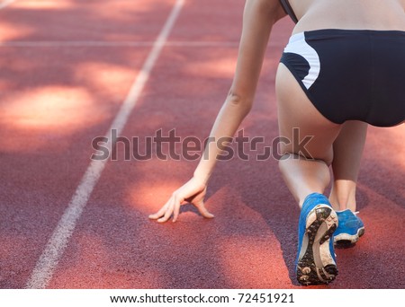 Female athlete/sprinter in \'on your marks, get set, go\' starting starting position, shot from behind.