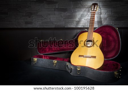 illuminated classic music guitar with case in front of leather and stone wall