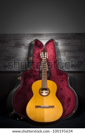 illuminated classic music guitar with case in front of leather and stone wall