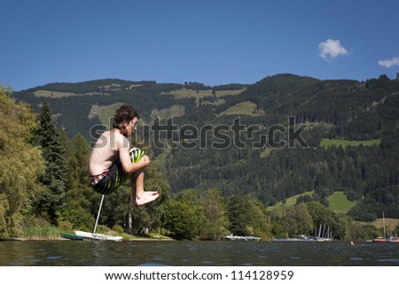 male teenager in the air while jumps in to a lake with nice nature in the back