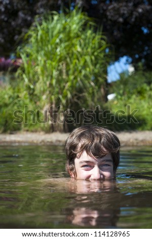 young boy is with half of his head in the water of lake zell am see with green bush in the back