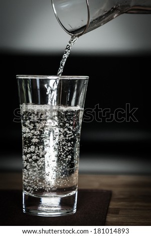 pouring some fresh clean water into glass with jug