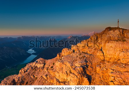 orange glowing rocks of mountain peak with cross at sunset