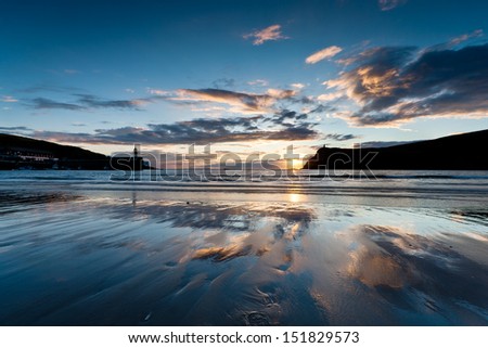 Sunset on Port Erin beach with Raglan Pier and Bradda Head in silhouette. The sky with golden clouds are reflected on the wet sand