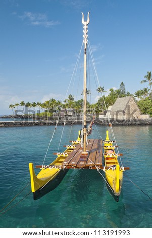 Traditional Hawaiian outrigger canoe lit by the early morning sun floating in a clear ocean water.