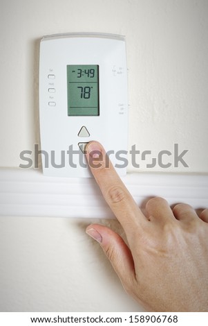 A woman\'s hand setting the room temperature on a modern digital programmable thermostat
