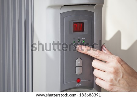 A woman\'s hand setting the room temperature on a modern digital programmable oil heater radiator