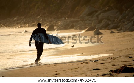 Surfer running on the beach at sunset