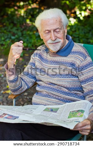 Elderly gentleman reading the newspaper outside in the garden.