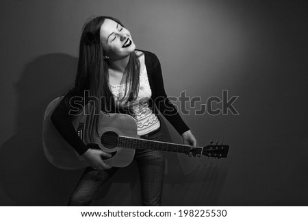 Young brunette playing the guitar in front of green background.