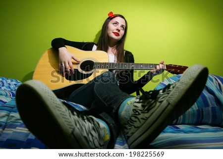 Young brunette playing the guitar on bed.