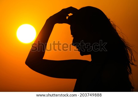 Silhouette of a woman running her hand through her hair at sunset.