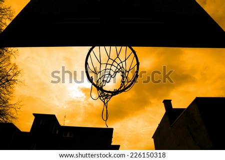 A silhouette of a basketball hoop shot from below with yellow sky..