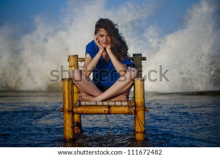 Beautiful and sexy woman staying on a old chair and  big waves are in the background from the ocean.