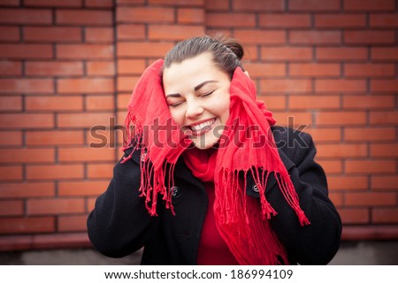 girl in a red scarf covers his ears with his hands. The girl was surprised and laughing. Closeup portrait against a brick wall.