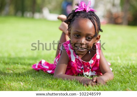 Outdoor portrait  of a cute little African american girl lying down on the grass