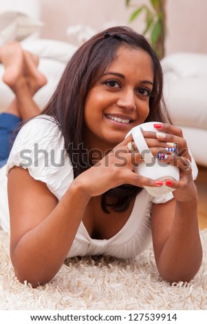 Young beautiful indian woman drinking coffee , lying on the floor while