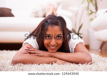 Young happy indian woman lying down on the floor in the living room