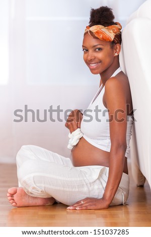 Young pregnant black woman seated on the floor touching her belly- African people