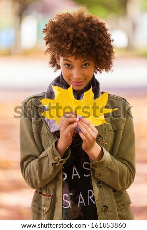 Autumn outdoor portrait of beautiful African American young woman holding yellow leaves - Black people