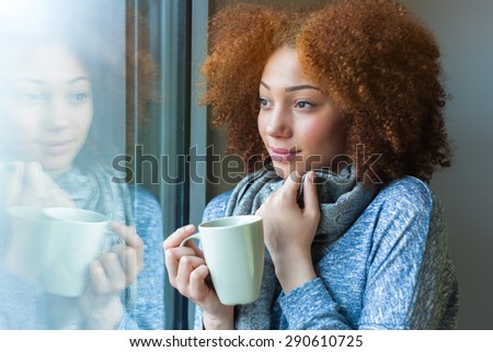 Black African American teenage girl drinking a hot beverage and looking through a window
