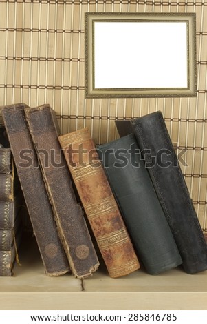 Front view of old books stacked on a shelf. Books without title and author. Old picture frame for your text.