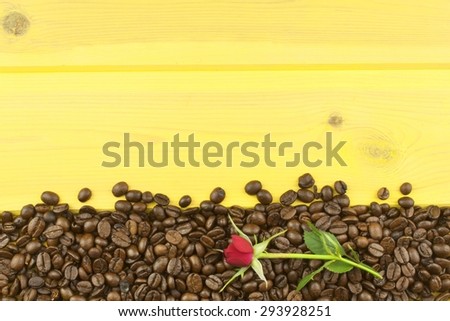 We love coffee. Roses resting on the coffee. Coffee beans, poured out on Yellow wooden table. Background for your text.