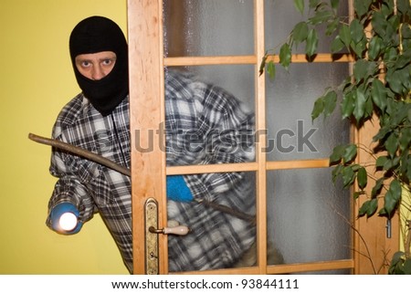burglar in mask breaking into a house through door