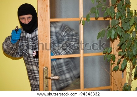 burglar in mask breaking into a house through door, with gun