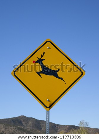 A deer crossing warning sign with a red sticker on the nose to make the deer look like Rudolph the red-nosed reindeer.