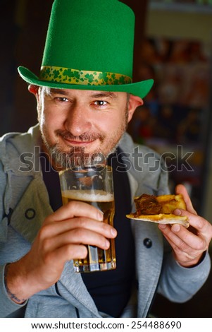 Funny Irishman in the national hat, drinking beer, eating pizza