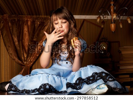 Little girl in a blue dress on the floor in a little room eat cake