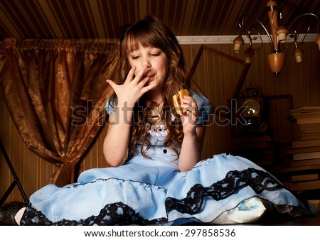 Little girl in a blue dress on the floor in a little room eat cake