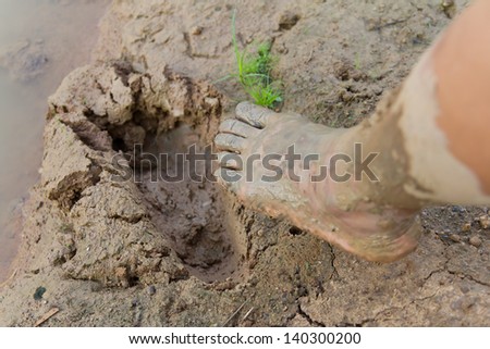 Footprints in the mud, and the feet of a man about to step on it.