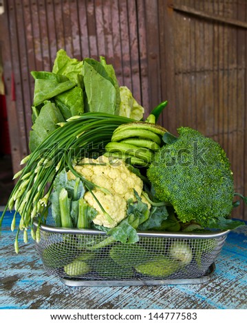 Group of green leaf vegetables grill basket with steel door as a backdrop.