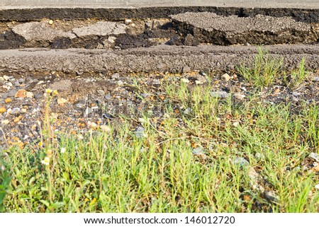 Side asphalt road broken due to collapsing ground until the grass grows