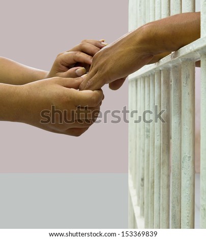 Woman comforting man in prison by holding his hand gently