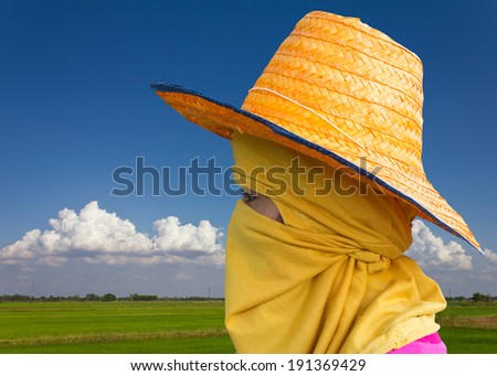 Farmer woman wearing a hat and a veil amid field and sky with clouds.